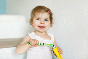 Choosing the Best Toothpaste for Kids illustrated by a baby holding a toothbrush and tube of toothpaste