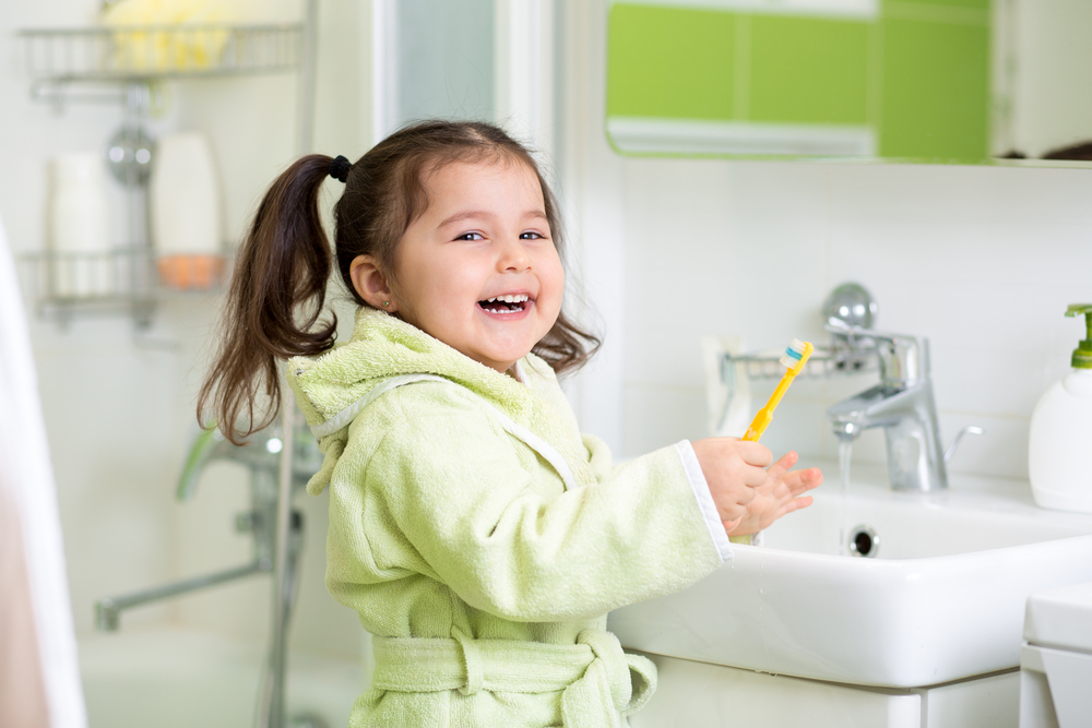 kid smiling while brushing her teeth
