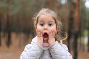 Girl with hands on face and mouth open for a post on bad breath in kids