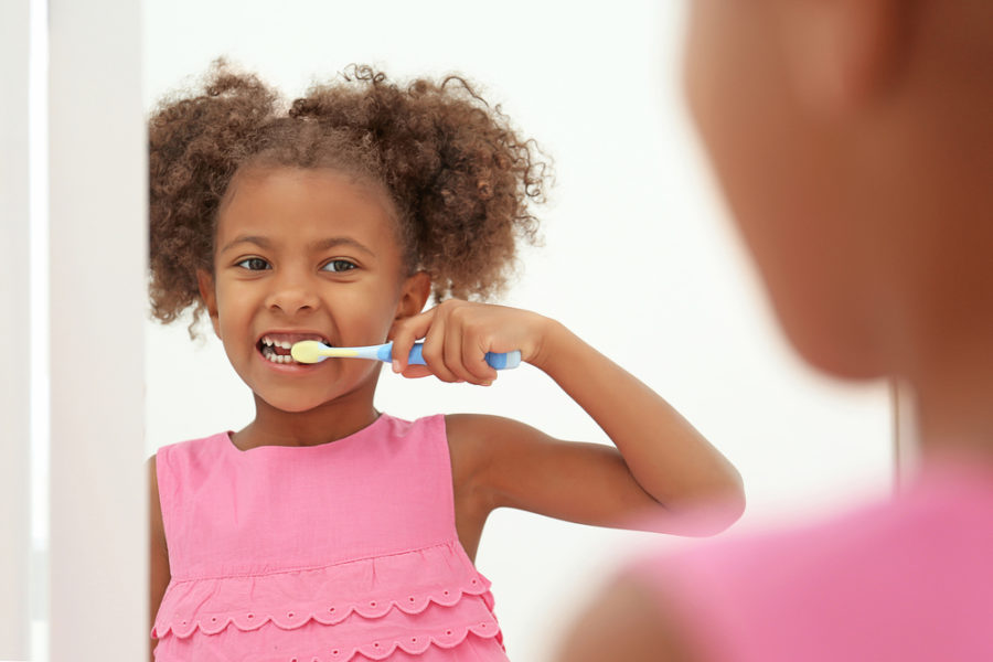 Cute African American Girl Brushing Teeth And Looking In Mirror